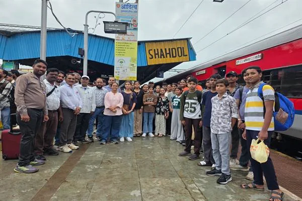 शहडोल रेलवे स्टेशन के प्लेटफॉर्म पर 'SHAHDOL' बोर्ड के नीचे खड़े स्कूली खिलाड़ियों और अधिकारियों का समूह, बगल में खड़ी लाल-सफेद ट्रेन।
